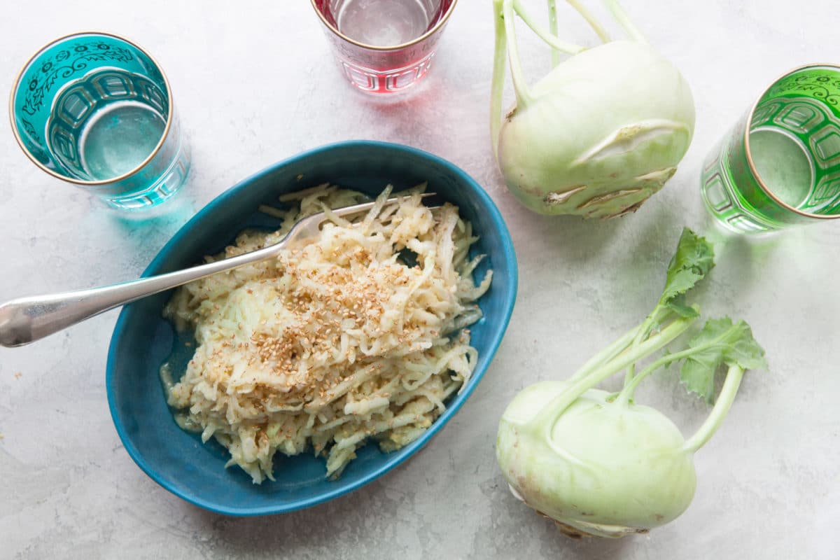 Dish of Asian Kohlrabi and Apple Slaw on a table next to whole kohlrabies.