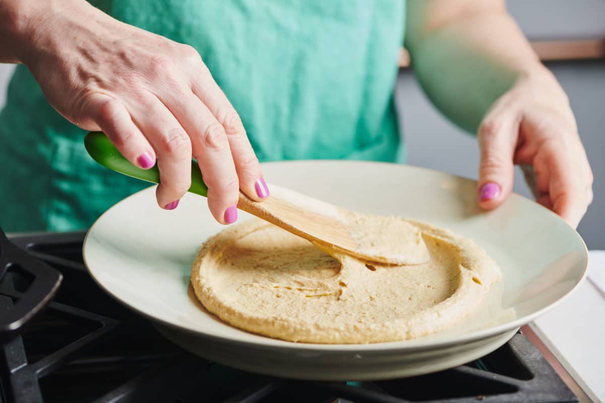 Woman spreading hummus onto a plate.