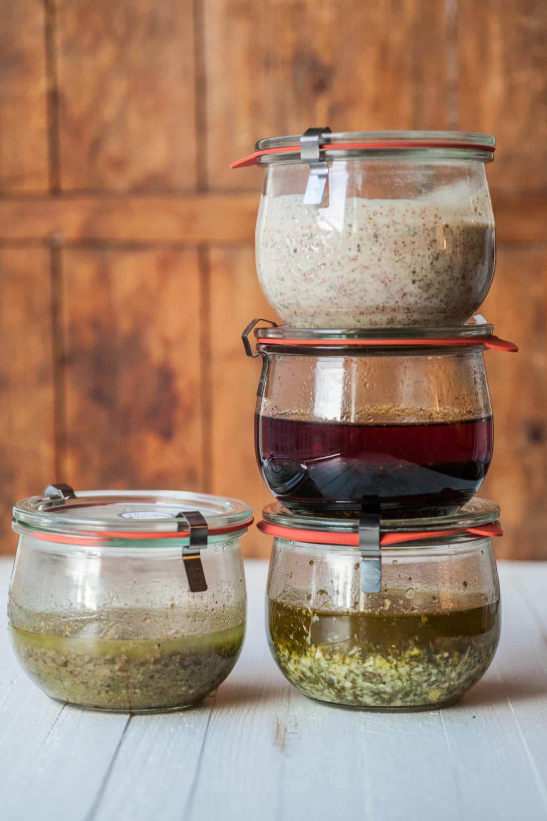 Four marinades in jars stacked on wood counter.