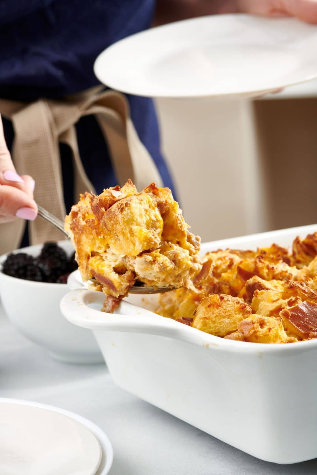 Woman scooping Savory Challah Bread Pudding from a baking dish.