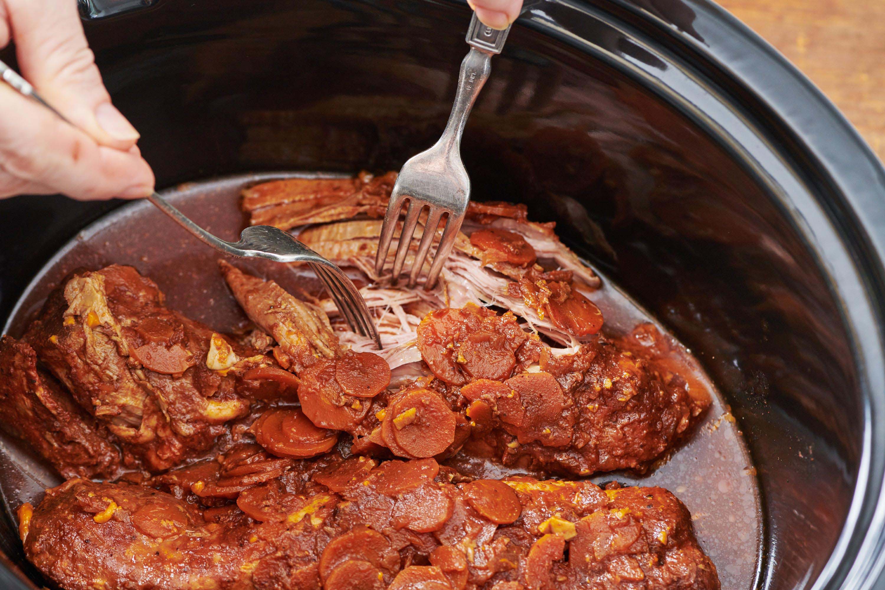 Pulling pork loin apart with forks in slow cooker.