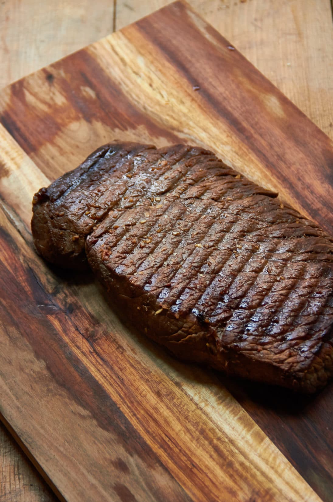 Grilled Marinated London Broil resting on a wooden surface.