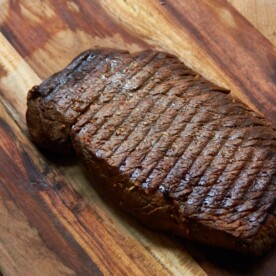 Grilled Marinated London Broil resting on a wooden surface.