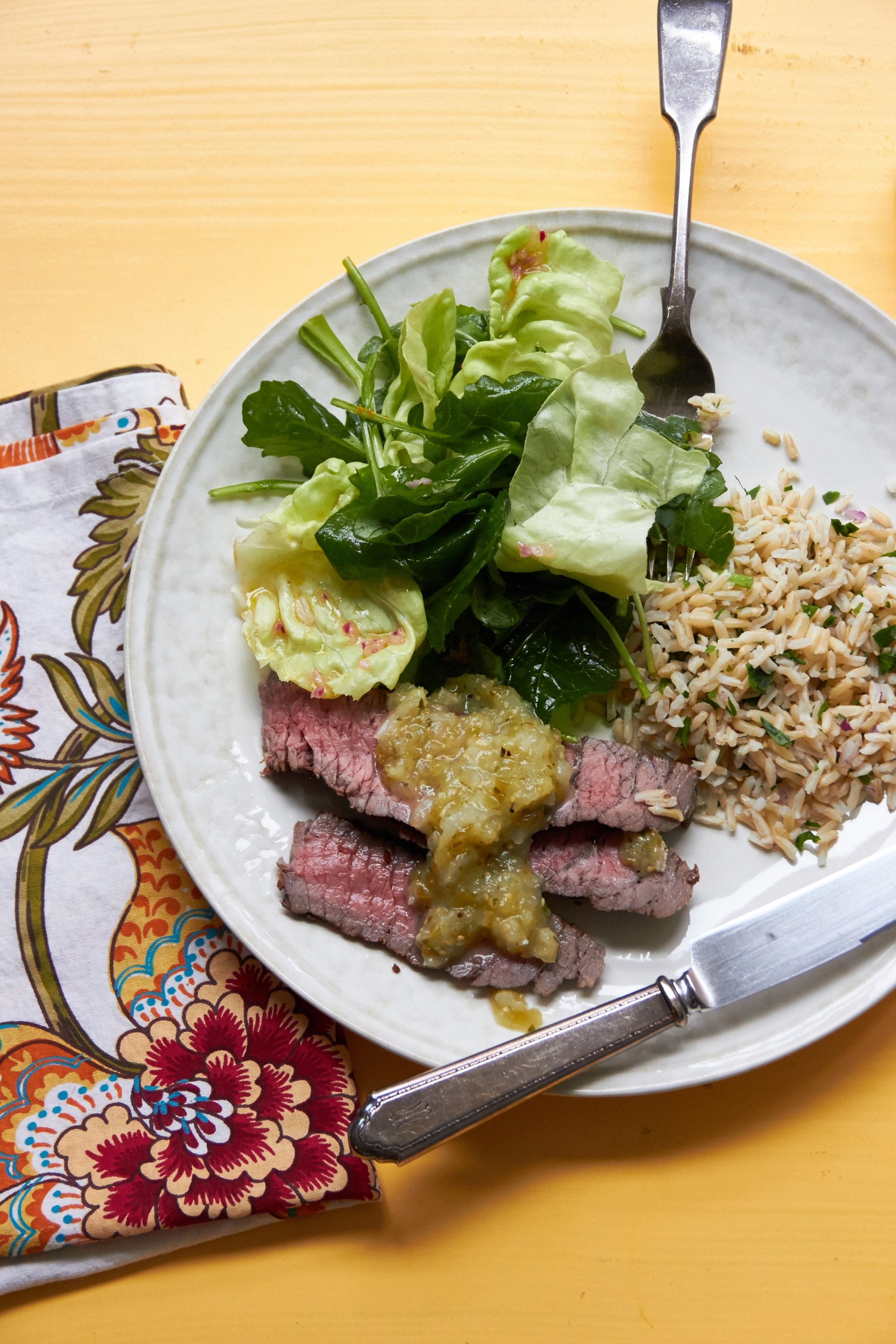 Grilled Marinated London Broil on plate with sauce, rice, and salad.