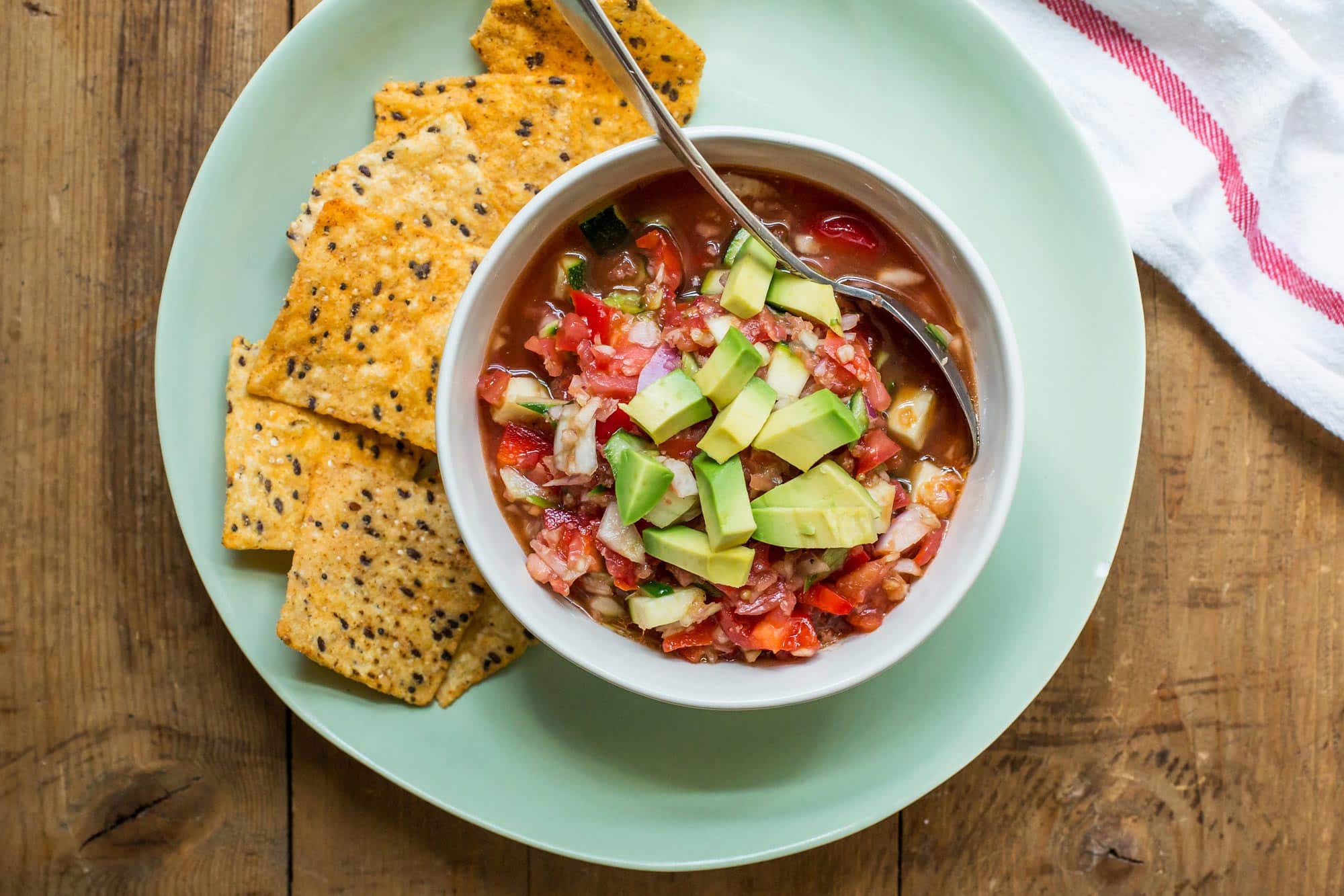 Gazpacho in a bowl on a plate with some tortilla chips.
