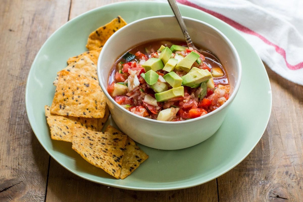 Green bowl with Gazpacho topped with avocado and tortilla chips on the side.
