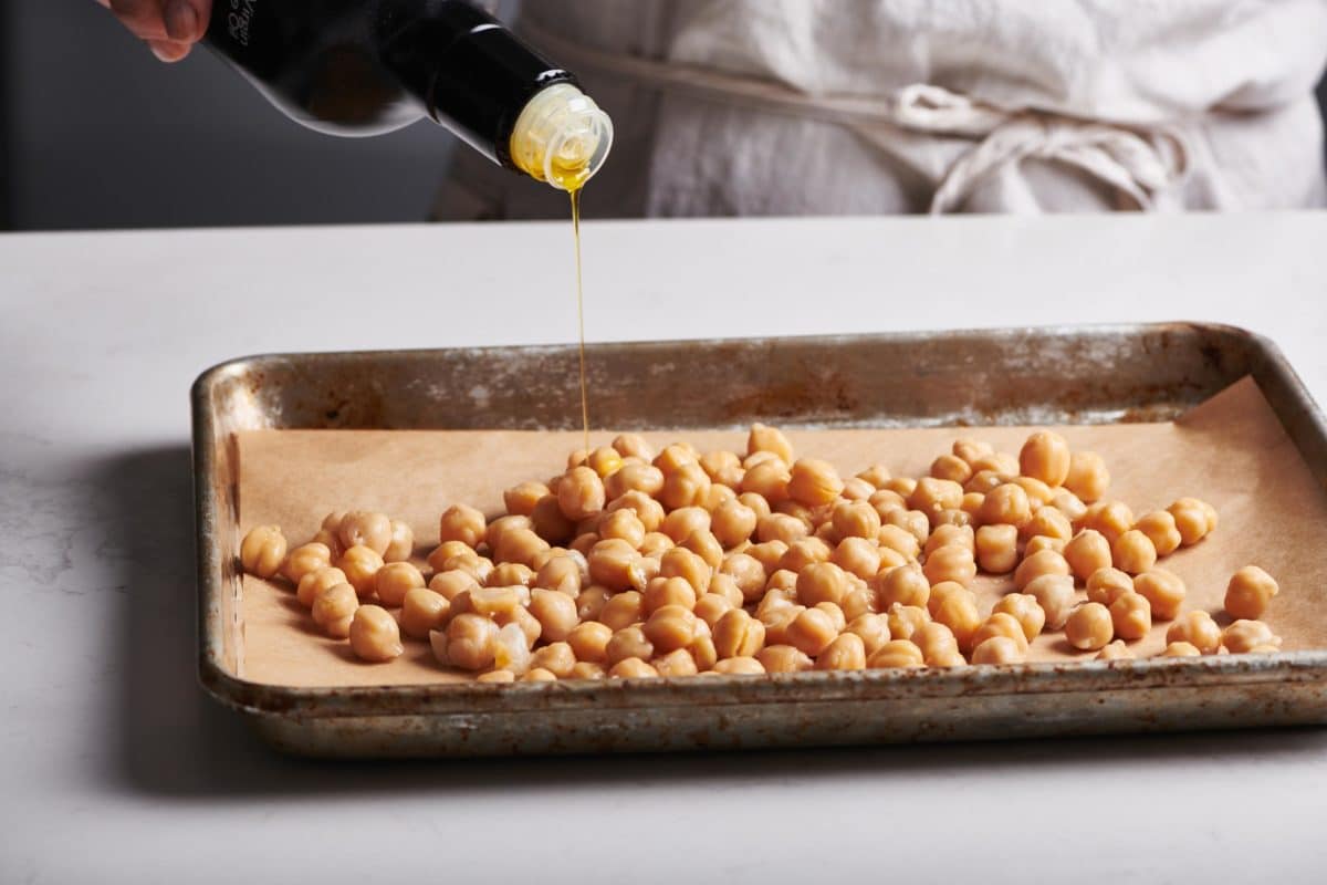Oil drizzling onto a lined baking sheet of chickpeas.