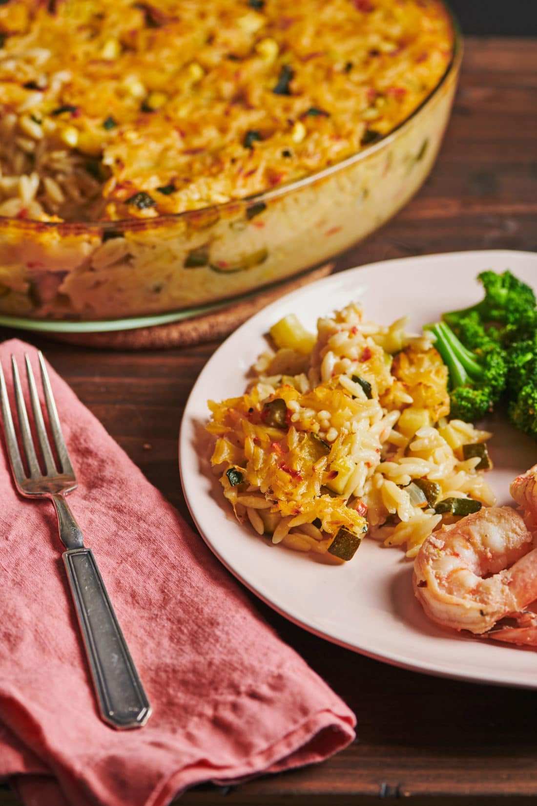 Cheesy Orzo Casserole on a plate with broccoli and shrimp.