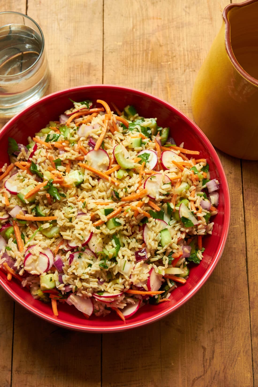Vegetable and Brown Rice Salad in red bowl on wood table.