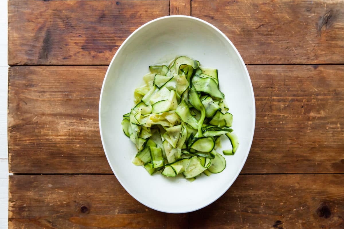 White serving plate of Zucchini Ribbon Salad on a wooden table.