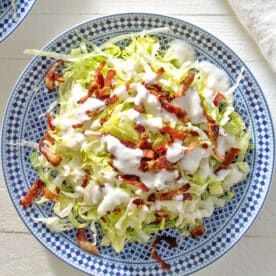 Chopped wedge salad on blue and white plate with buttermilk dressing and bacon.