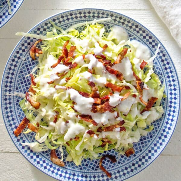 Chopped wedge salad on blue and white plate with buttermilk dressing and bacon.