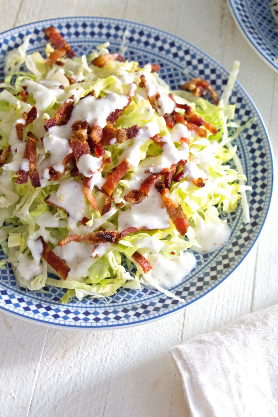 Slivered Wedge Salad with Buttermilk Dressing and Bacon on a blue and white plate.