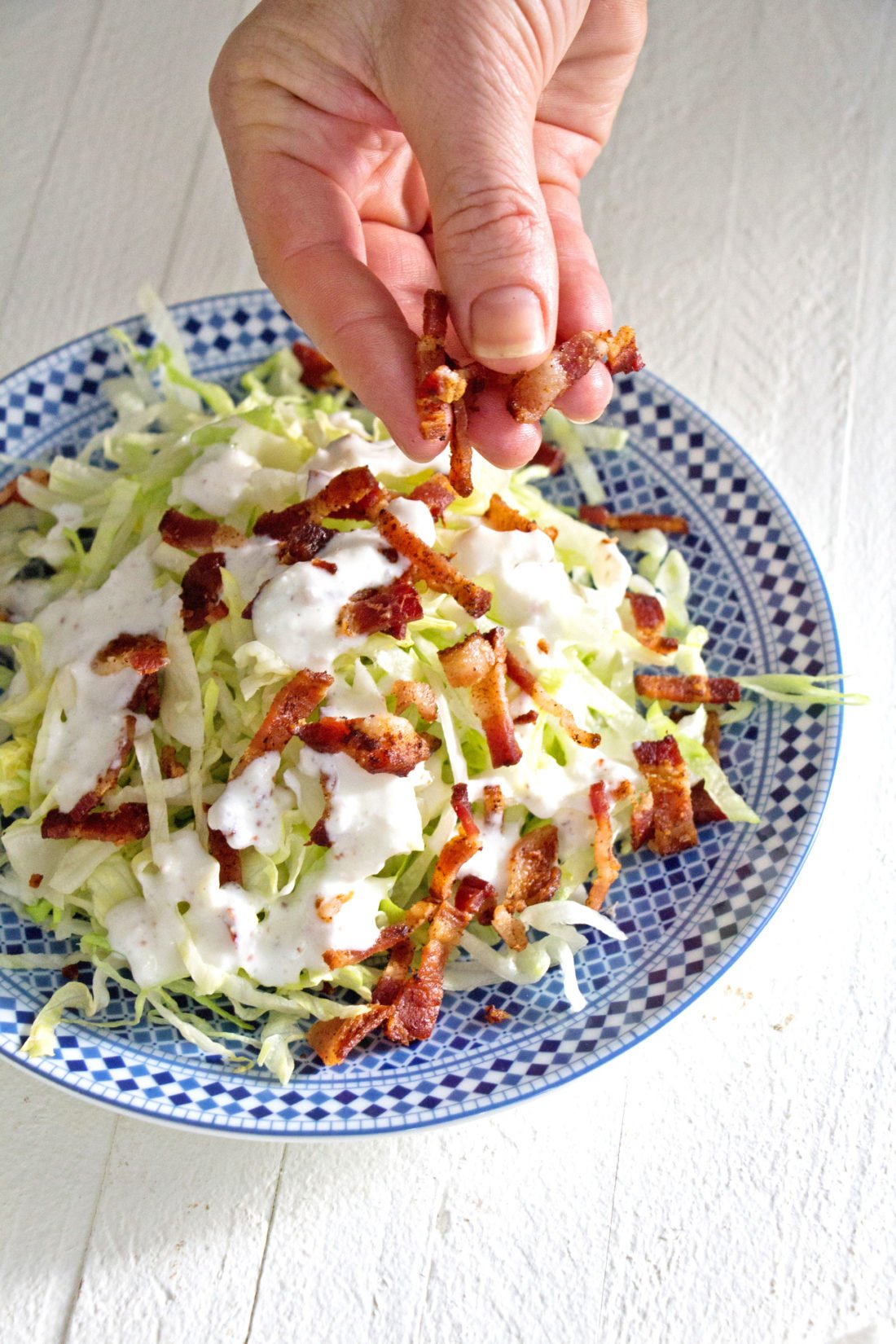 Woman sprinkling bacon onto a Slivered Wedge Salad with Buttermilk Dressing.