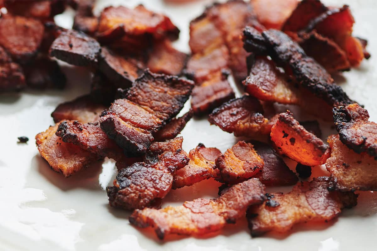 Cooked bacon lardons on white plate.
