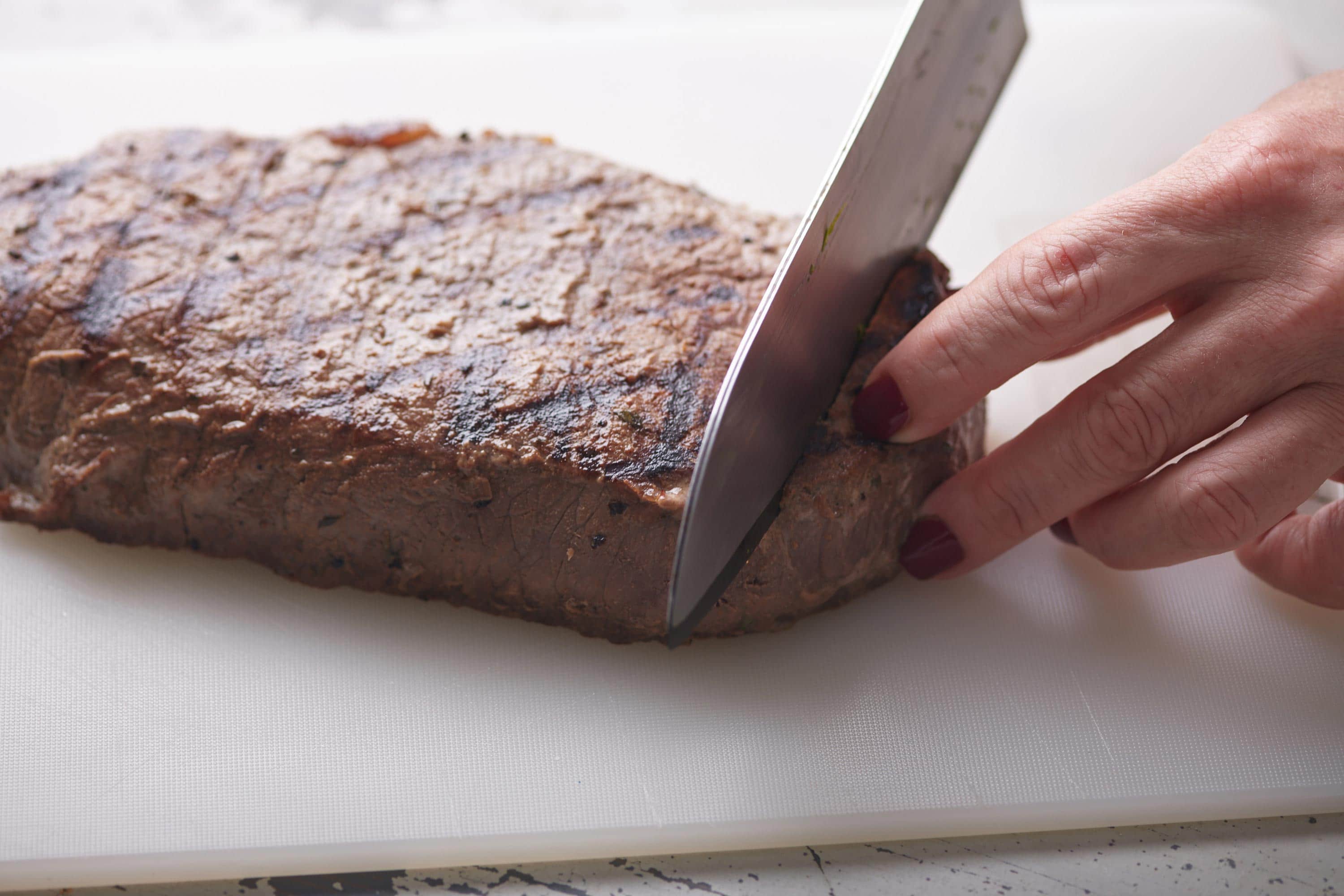 Woman slicing a Mustard Marinated London Broil on a cutting board.