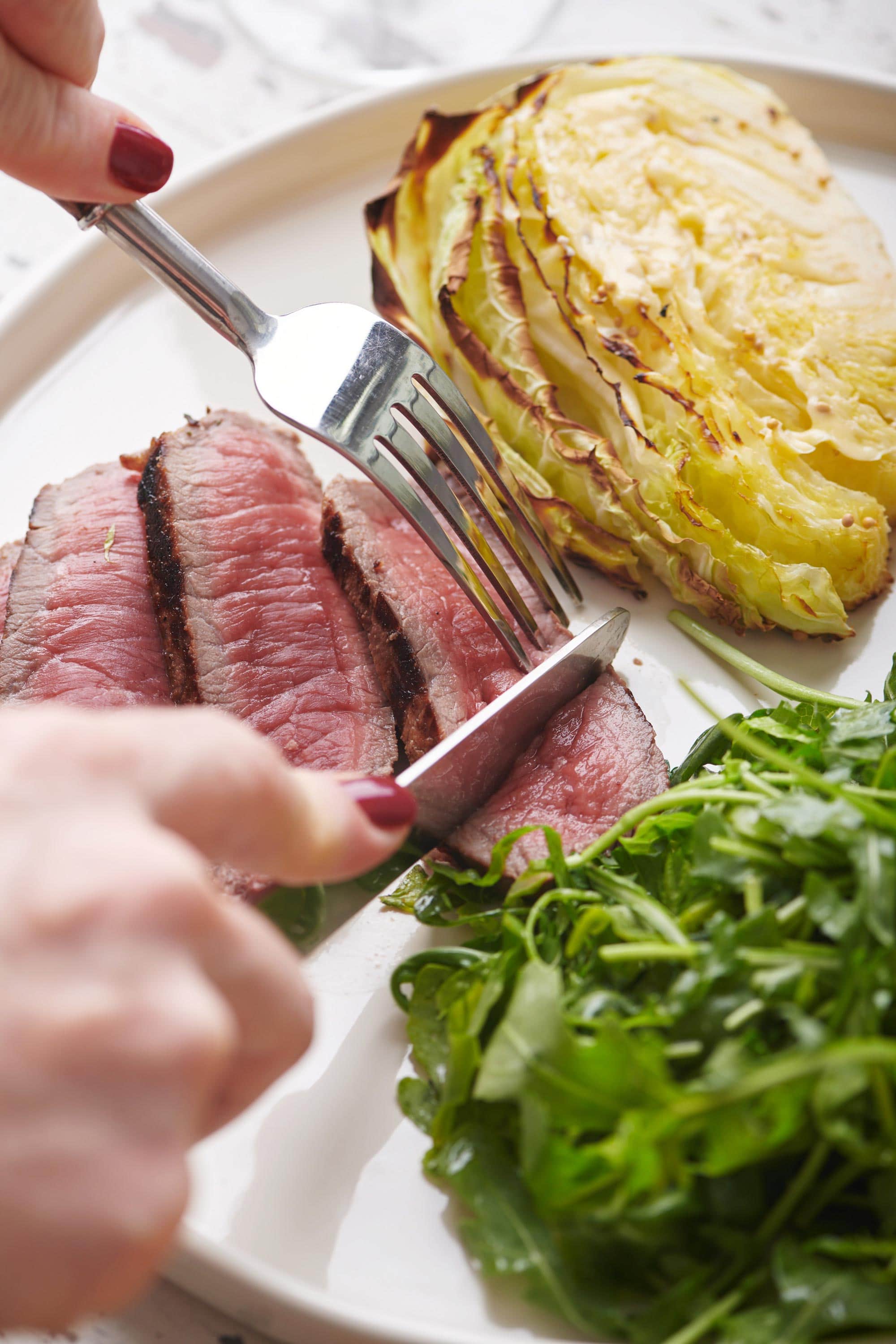 Woman using a fork and knife to cut a slice of Mustard Marinated London Broil.
