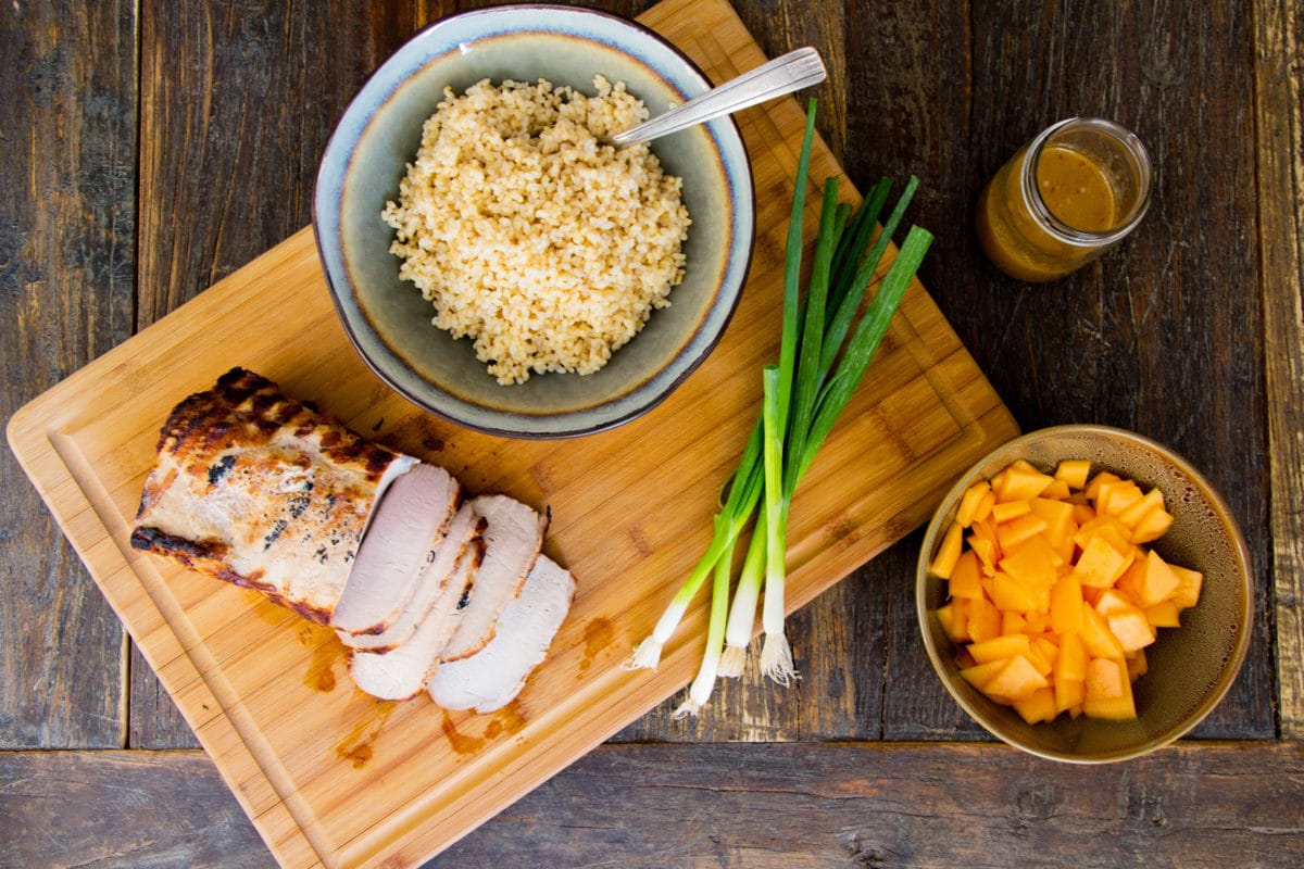 Grilled Pork Loin, brown rice, and green onions on a wooden cutting board.