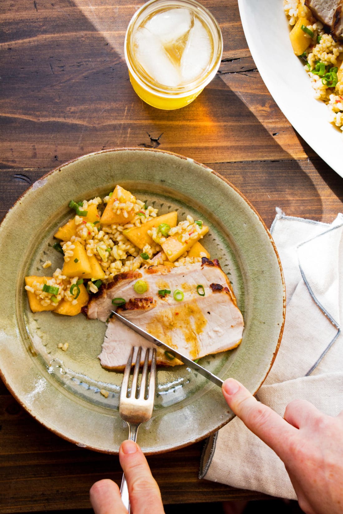 Person cutting a piece off of Grilled Pork Loin with Brown Rice Salad.