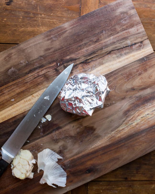 Bulb of garlic that is wrapped in foil and on a wooden cutting board.