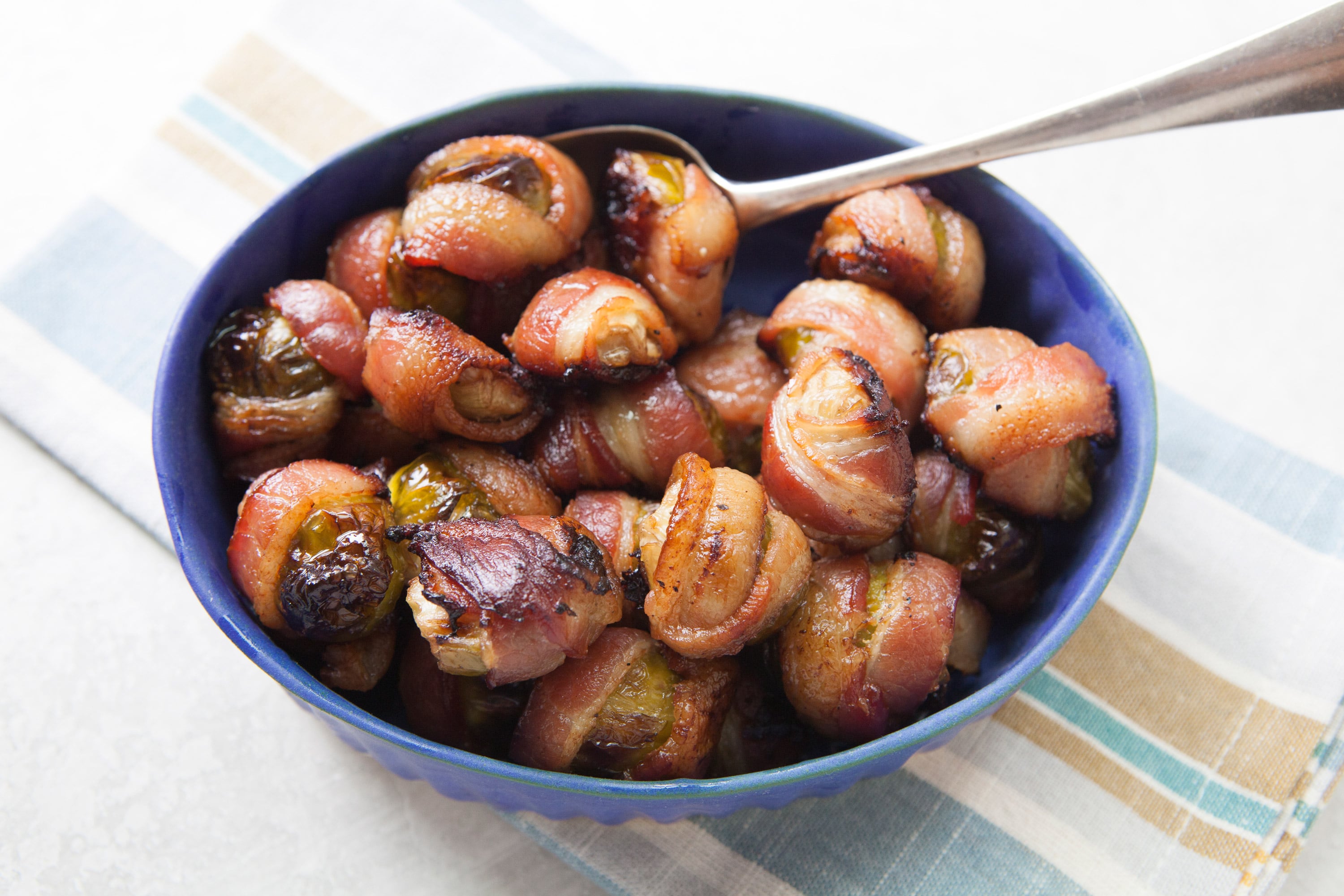 Bacon Wrapped Brussels Sprouts in blue bowl with serving spoon.