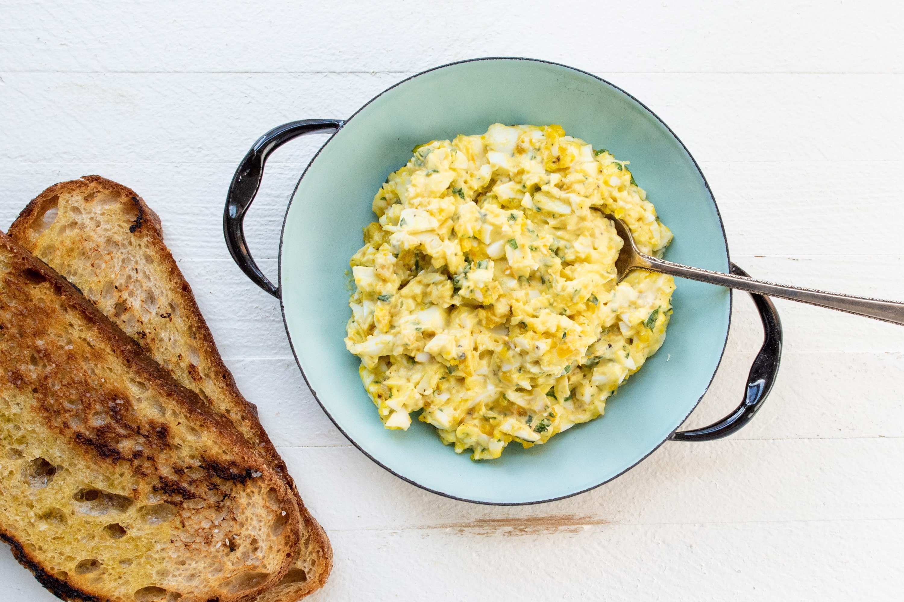 Egg Salad in a blue bowl with toast next to it.