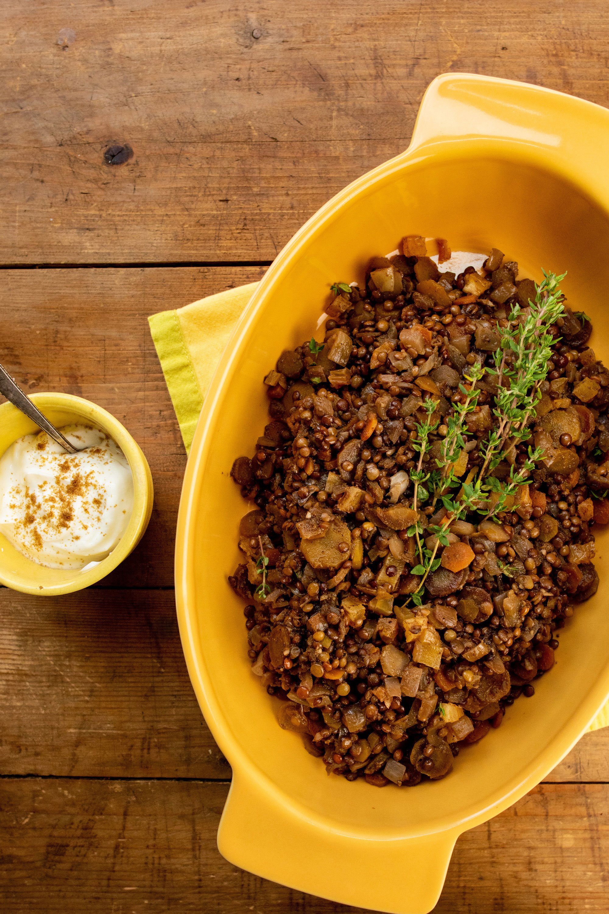 Lentils and Carrots with Dried Apricots in a yellow serving dish o a wooden surface with a little bowl of yogurt.