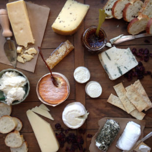 Wooden surface topped with cheeses, breads, and spreads.