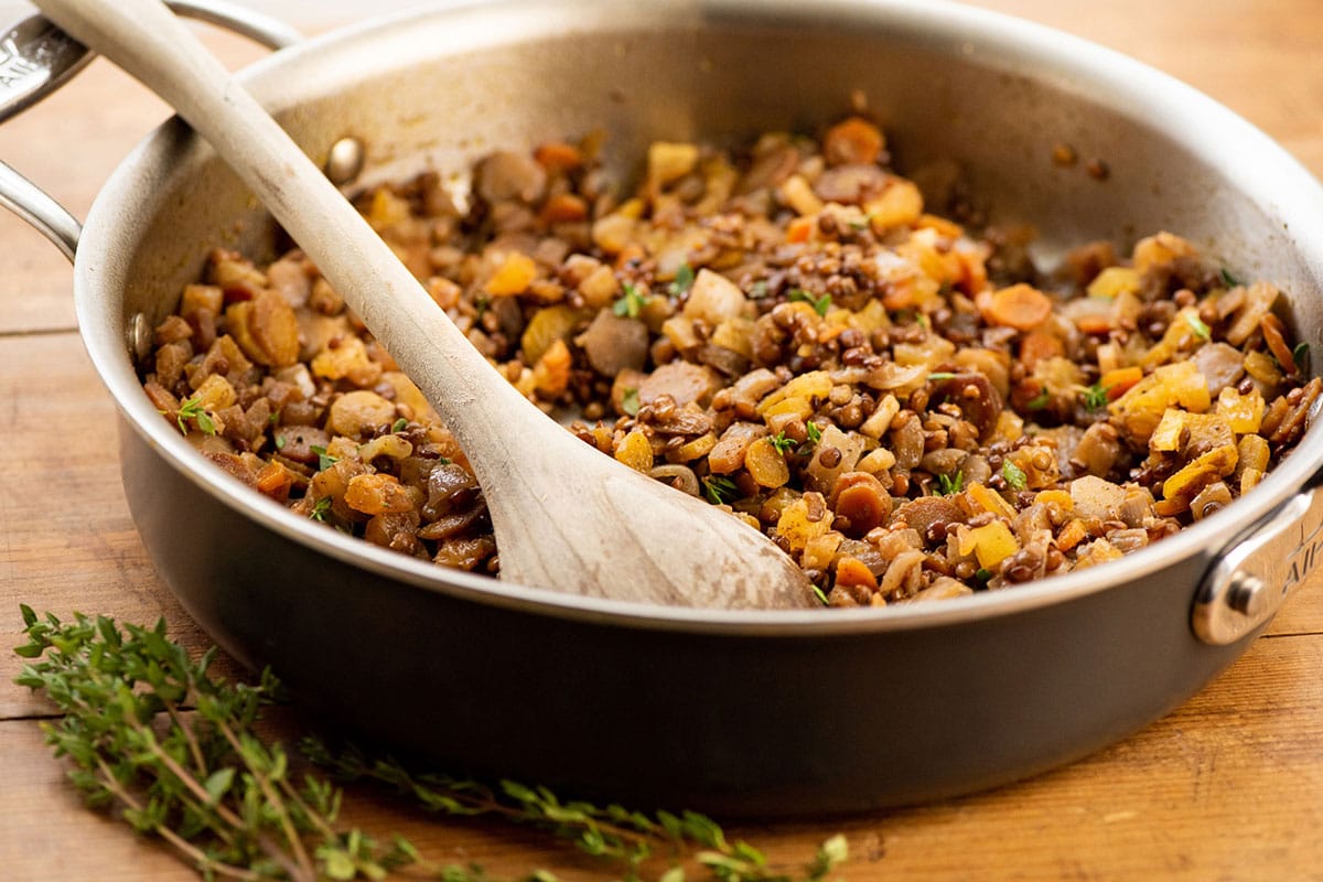Frying pan filled with Lentils and Carrots with Dried Apricots on table with wood spoon.