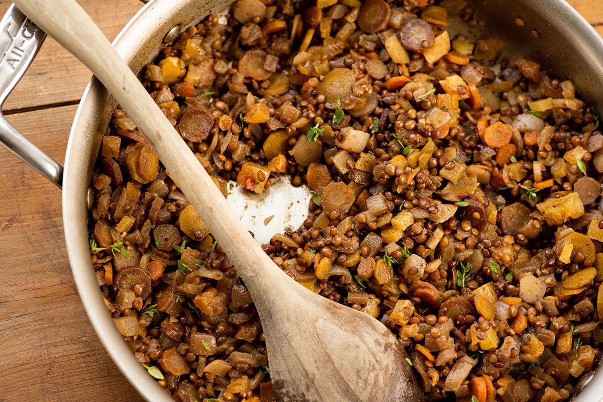 Lentils and Carrots with Dried Apricots being stirred with wooden spoon in pan.