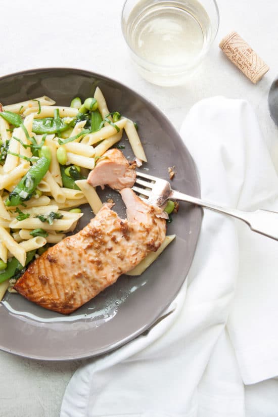 Table setting with horseradish-ginger salmon, penne and sugar snap peas, and a glass of wine.