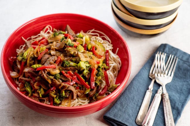 Red bowl of Spicy Stir Fried Beef and Vegetables over noodles.
