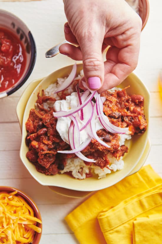 Woman adding slices of red onion to a bowl of Barbacoa Beef Chili.