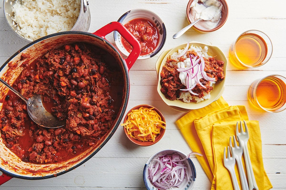 Barbacoa Beef Chili in pot on table with toppings in bowls.
