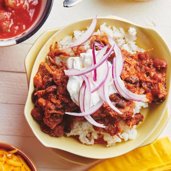Bowl of Barbacoa Beef Chili over rice topped with red onions and sour cream.