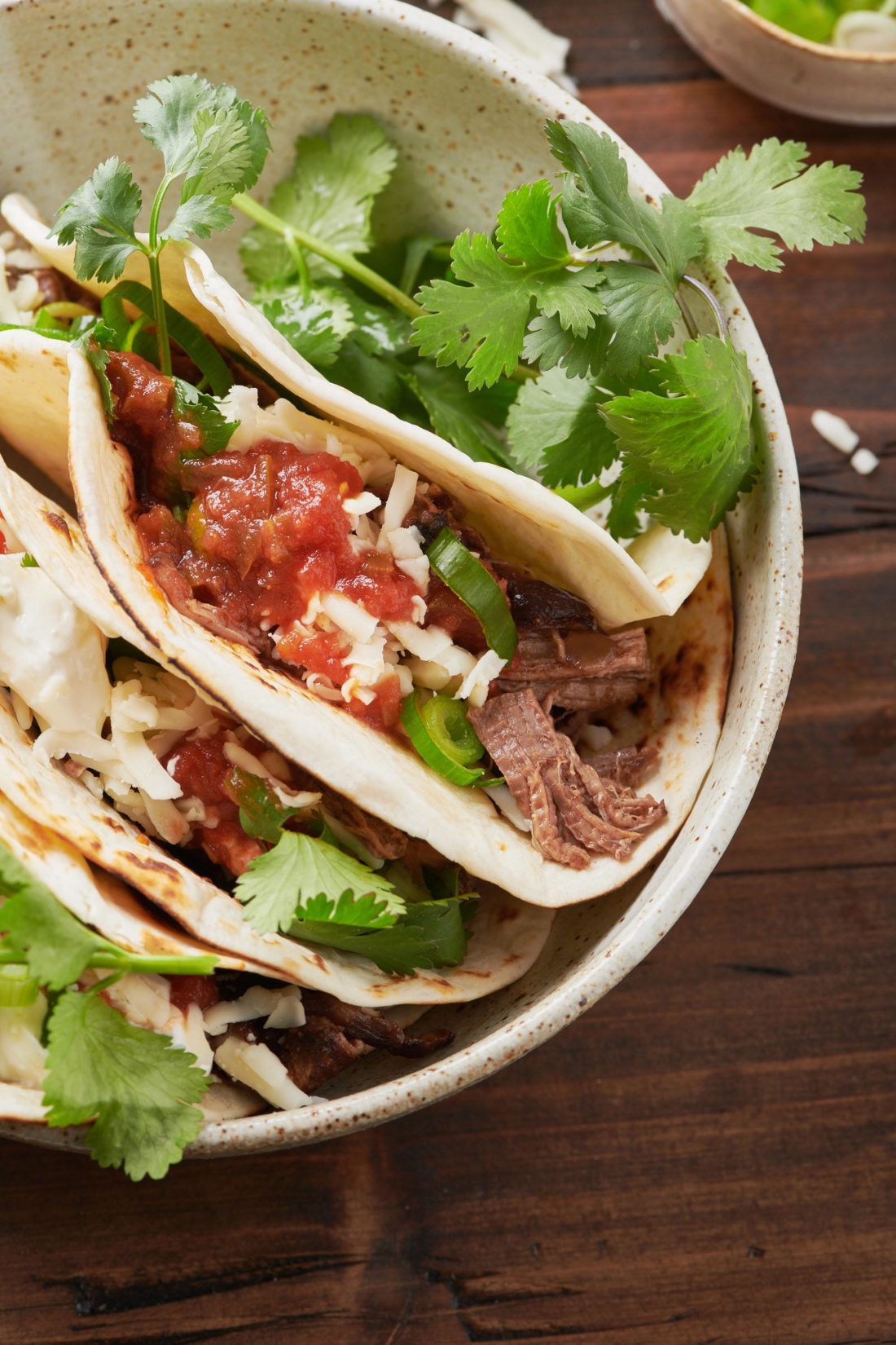 Barbacoa beef tacos topped with cheese, salsa, and cilantro.