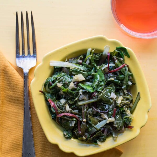 Yellow bowl with stir-fried Asian greens next to fork.