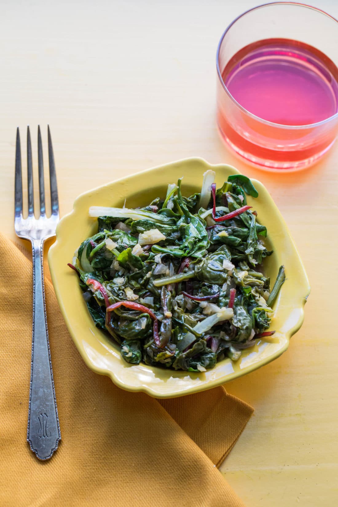 Clean and Spicy Asian Greens in yellow bowl next to red drink.