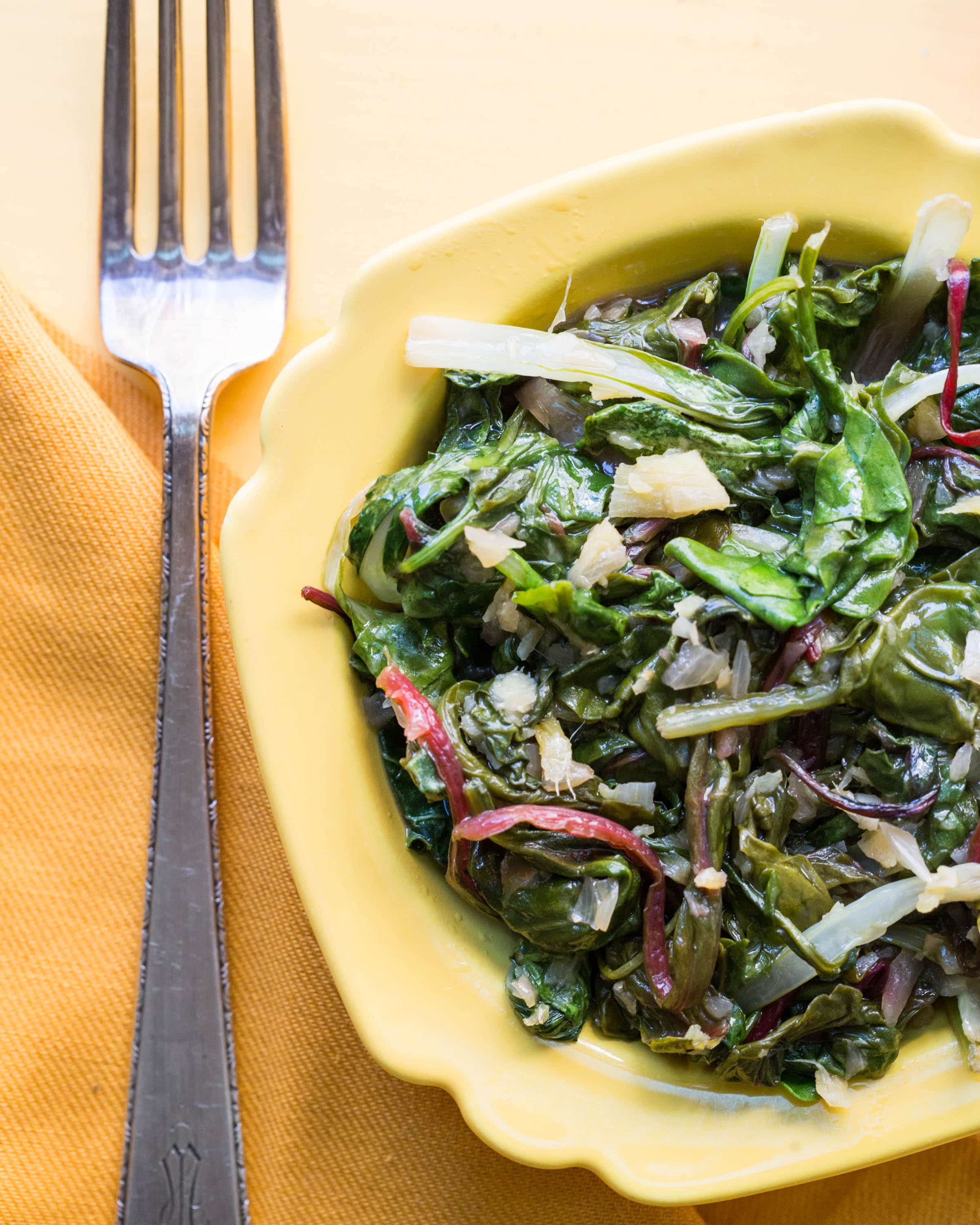 Yellow bowl with stir-fried Asian greens next to fork.