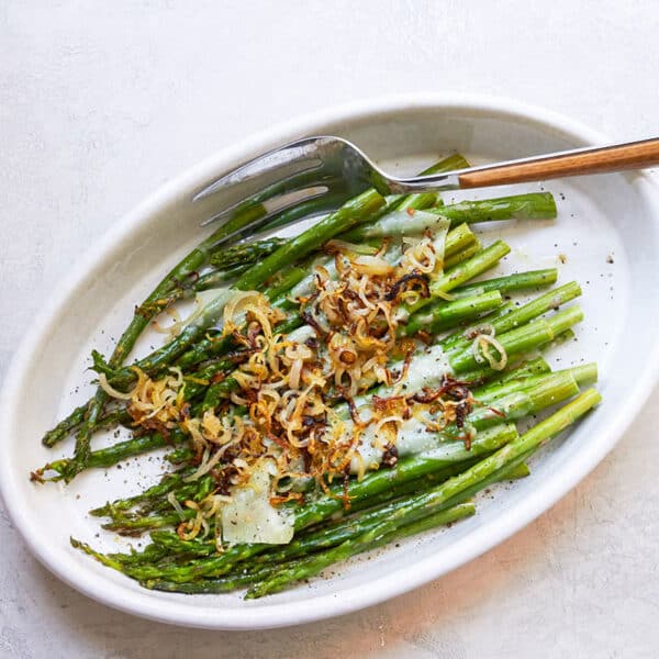 Roasted asparagus with crispy shallots and Parmesan on serving plate with spoon.