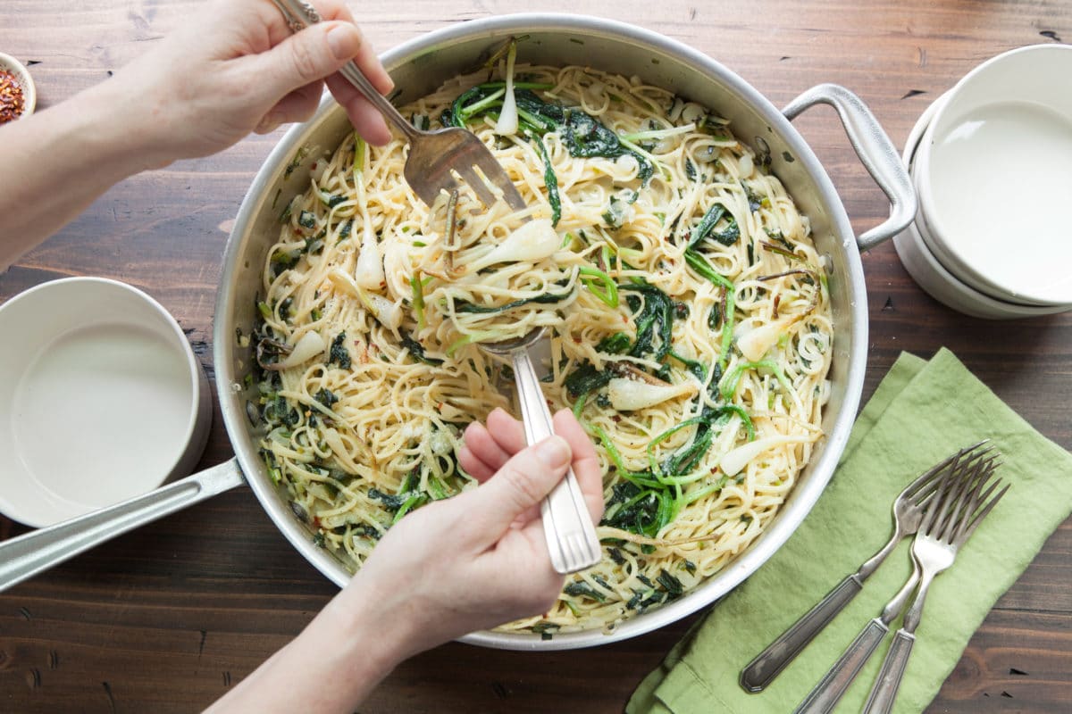 Person using a fork and a spoon to toss Ramp Pasta.