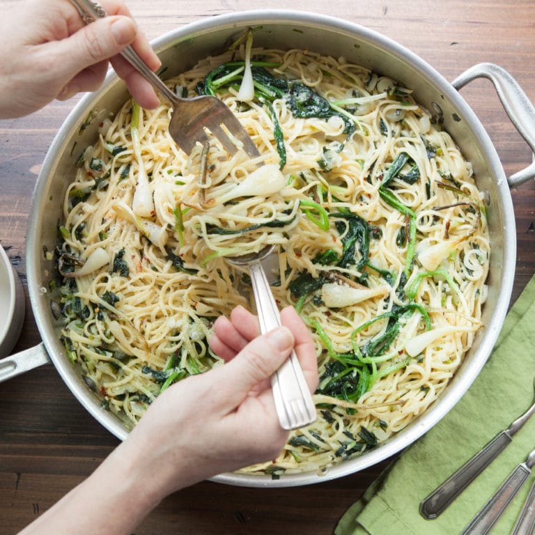 Person using a fork and a spoon to toss Ramp Pasta.