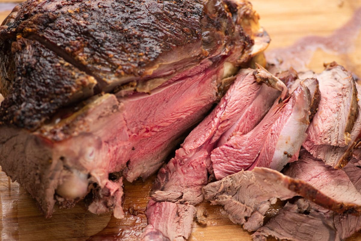 Partially-sliced Lemon-Garlic Semi-Boneless Leg of Lamb on a wooden surface.