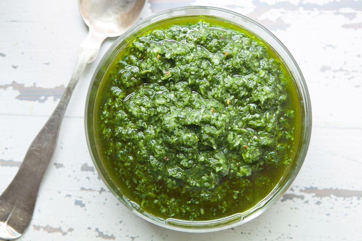 Ramp sauce in bowl next to spoon on white table.