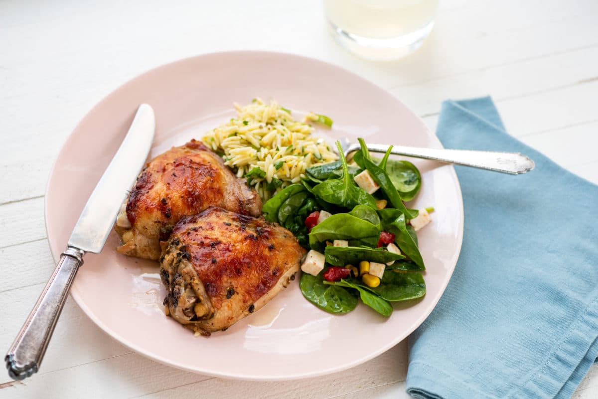 Greek Roasted Chicken Thighs with sides on pink plate.