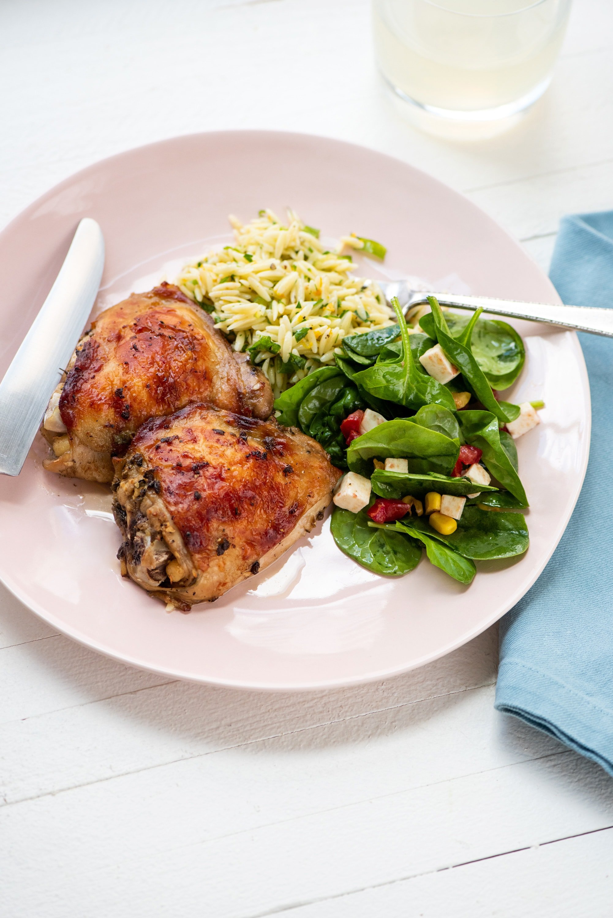Greek Roasted Chicken Thighs on a pink plate with orzo and salad.