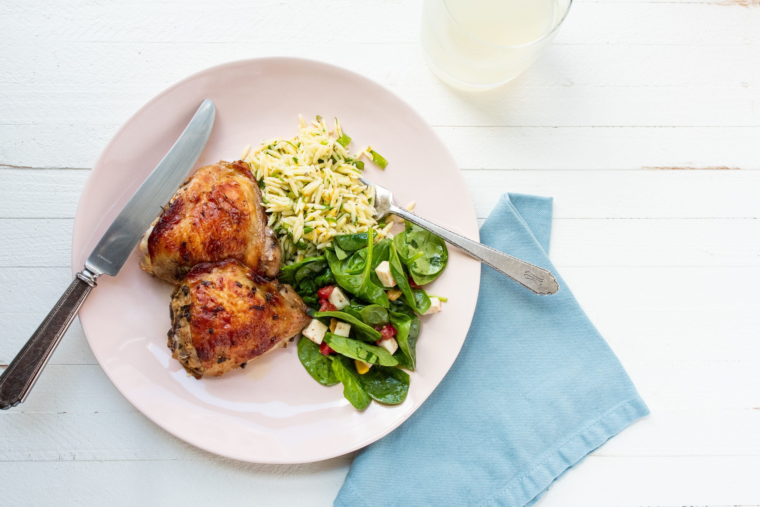Greek Roasted Chicken Thighs on plate with orzo side and green leafy salad.