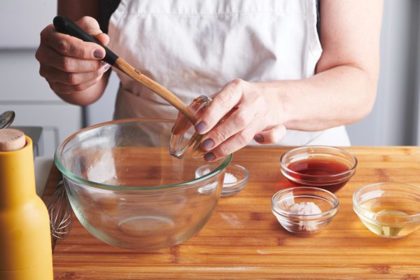 Woman scooping mustard into a glass bowl.