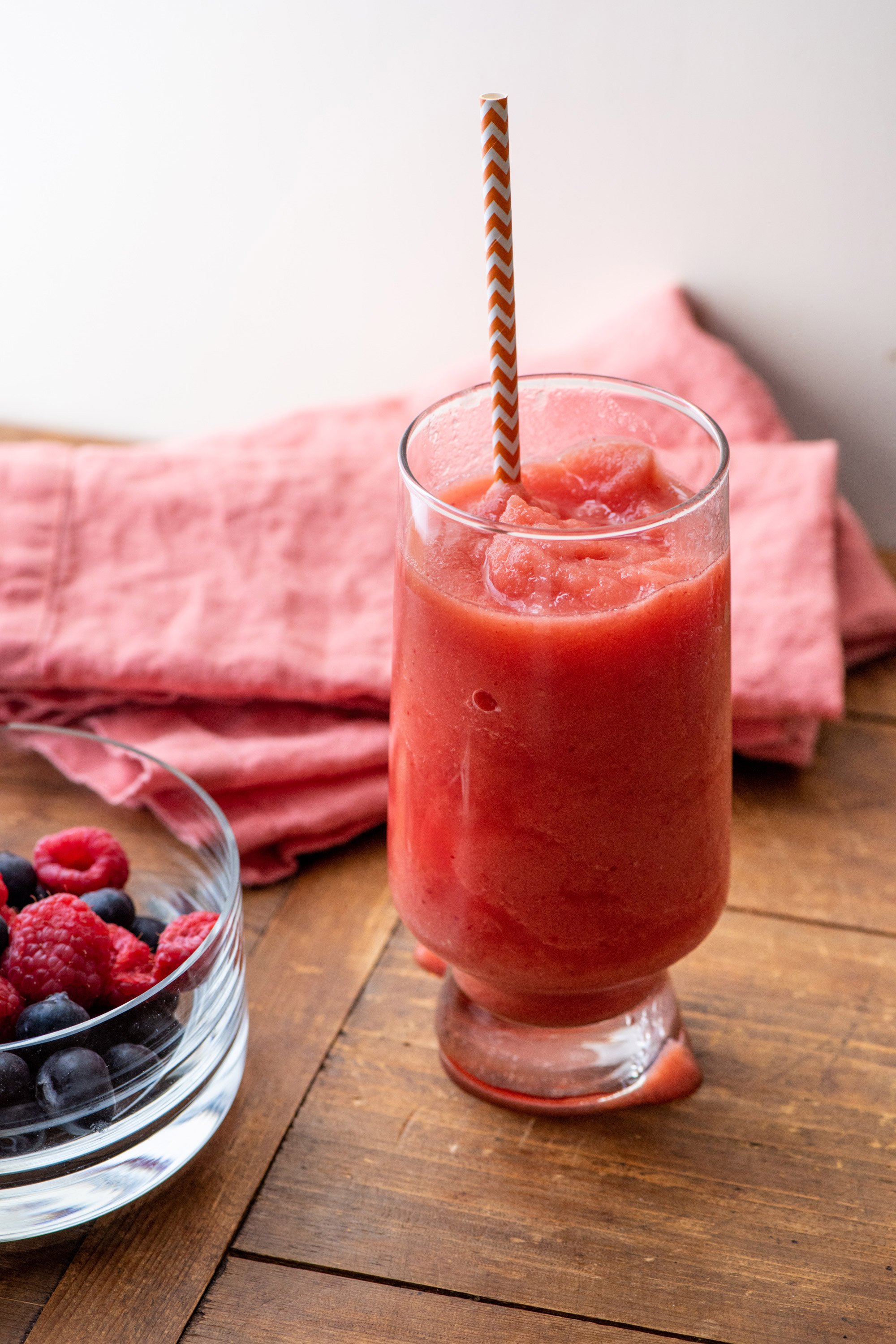 Glass of Watermelon Strawberry Smoothie next to a bowl of berries.