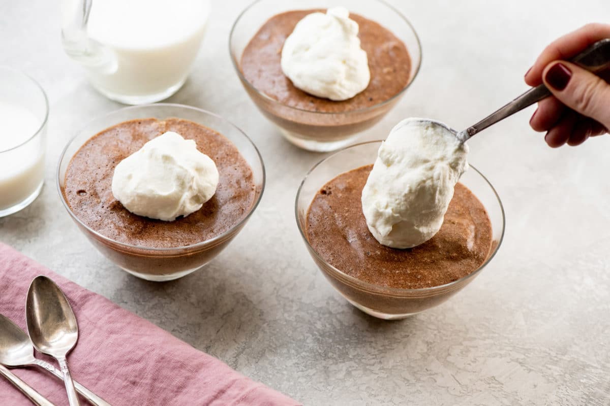 Spoon dolloping whipped cream onto dishes of Chocolate Mousse.